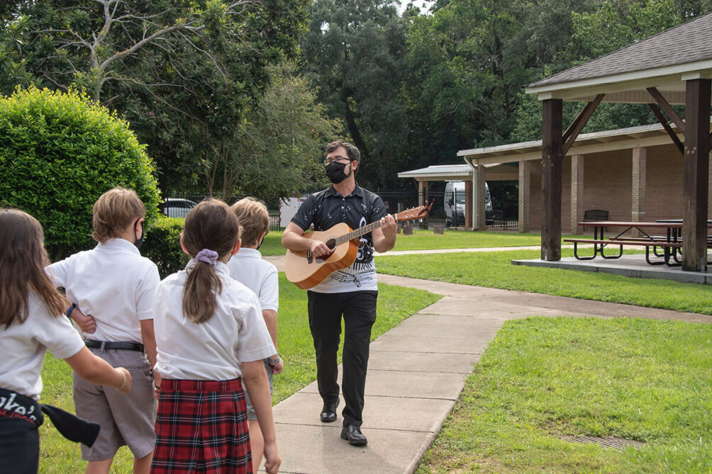 Mr. Driskell playing guitar and walking with St. Luke's students
